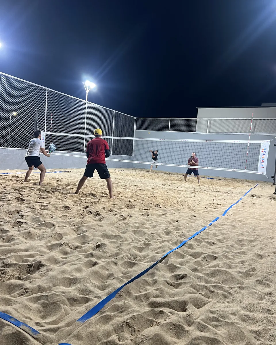 Amigos jogando beach tennis à noite na quadra de areia iluminada da Piccolini Eventos, em Goiânia