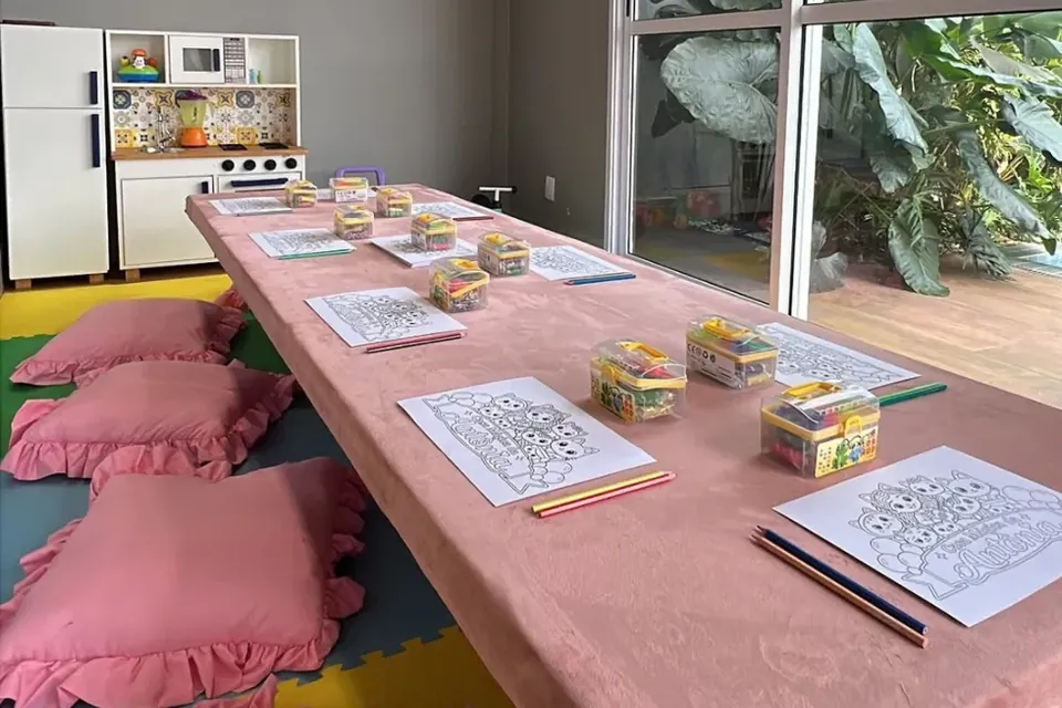 Brinquedoteca climatizada da Piccolini com mesa baixa, almofadas rosa, atividades de colorir e cozinha de brinquedo