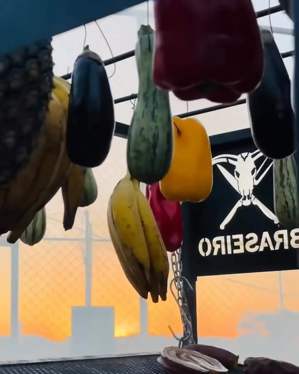 Linguiças e carnes na grelha com frutas penduradas ao pôr do sol no churrasco da Piccolini Eventos