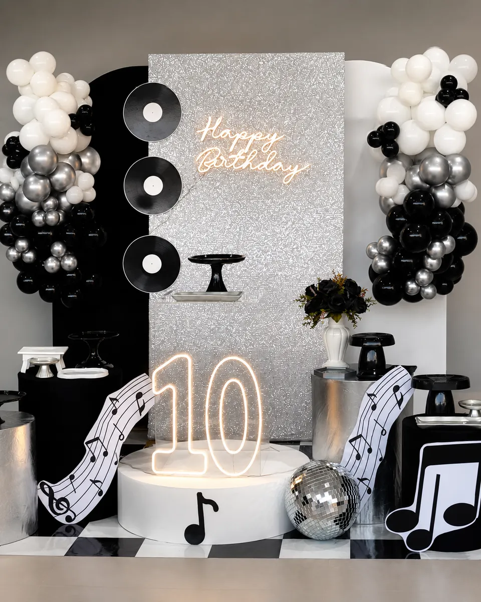 Painel de aniversário de 10 anos com tema musical, letreiro neon e balões preto, branco e prata na Piccolini