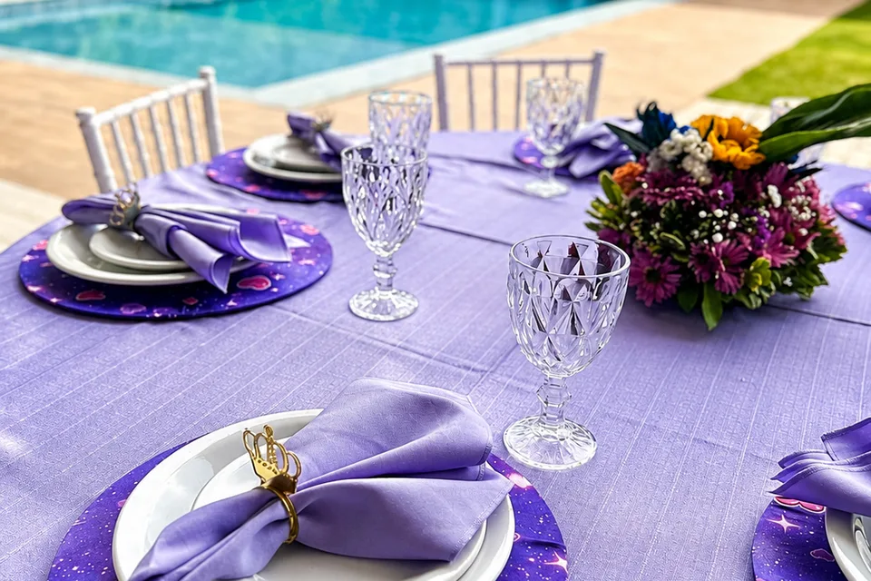 Mesa em lilás com sousplat personalizado e a piscina da Piccolini Eventos ao fundo