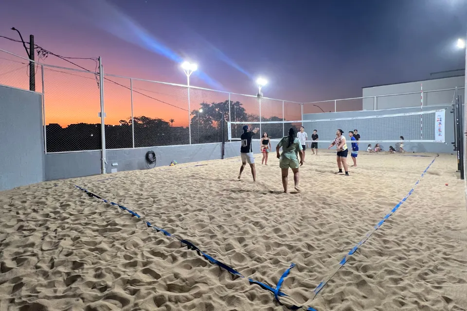 Quadra de areia iluminada da Piccolini Eventos, com jogo de vôlei ao entardecer, em Goiânia