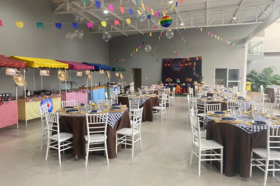 Salão da Piccolini Eventos montado para festa junina, com mesas redondas e cadeiras brancas
