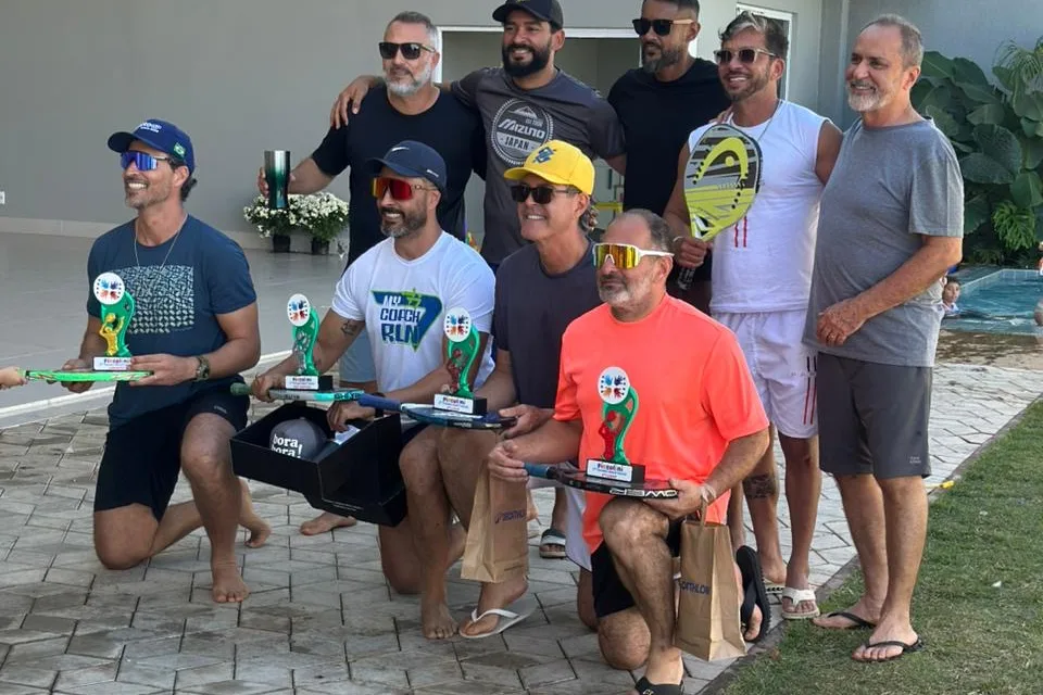 Jogadores reunidos com troféus e raquetes após o torneio de beach tennis na Piccolini Eventos